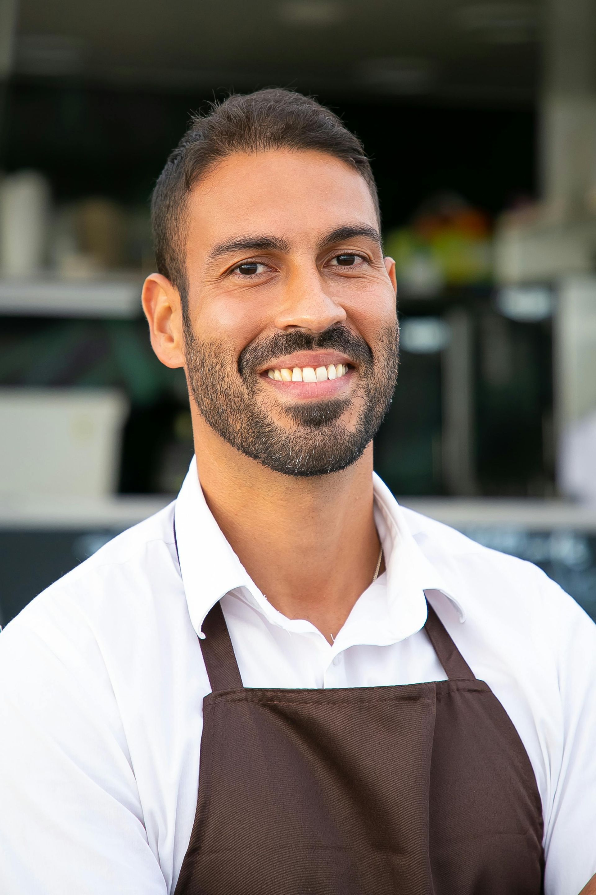 Smiling chef in a white shirt and brown apron standing in a kitchen setting