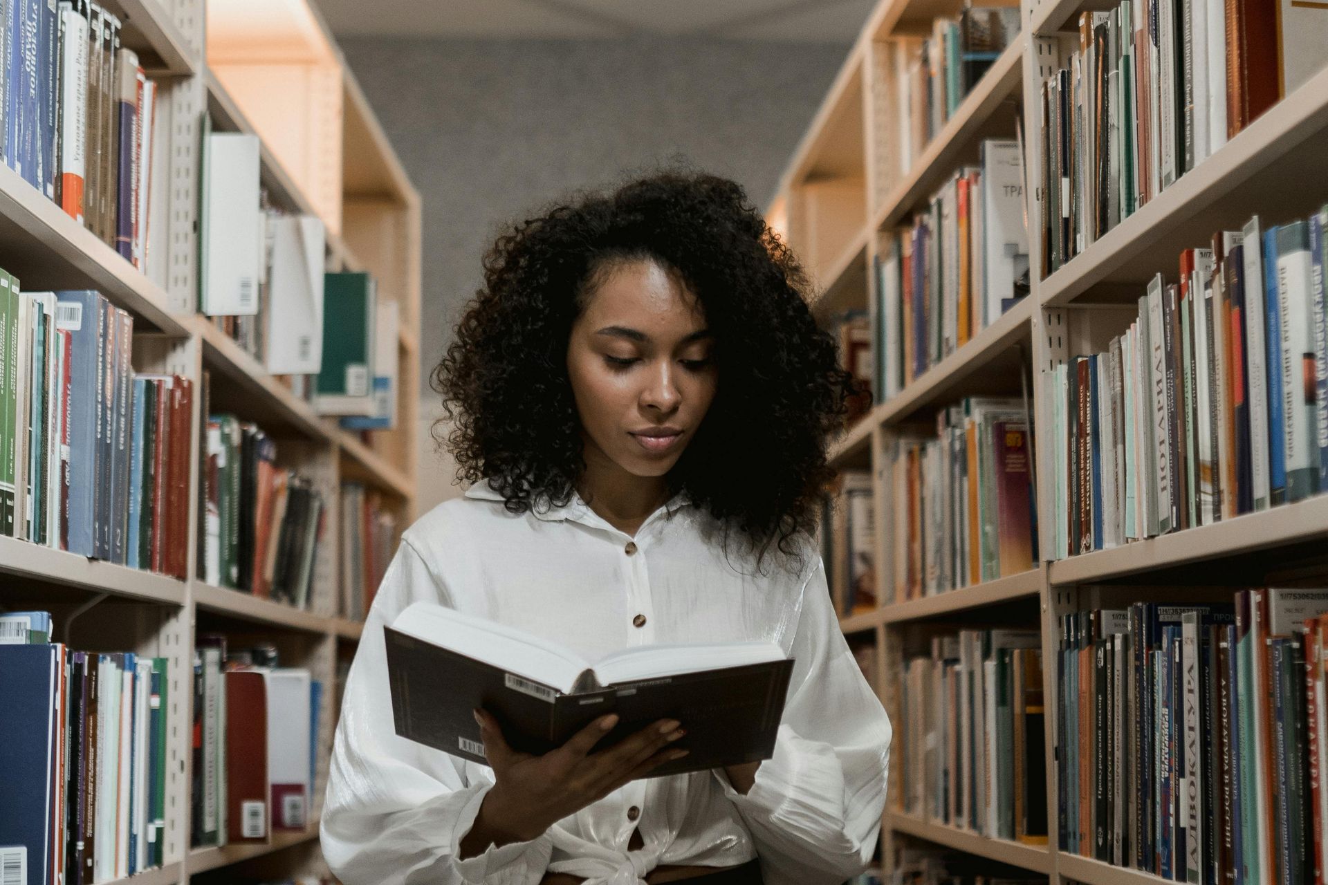 “Student reading a book in a library while preparing for academic success with guidance from Prestige Scholar.”