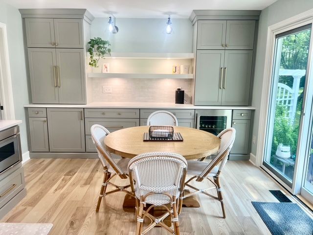 A dining area with a round wooden table, four woven chairs, light-gray cabinets, and hardwood floors.