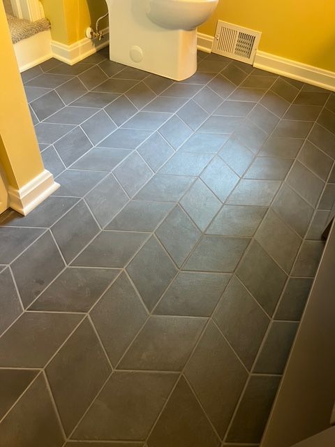 A bathroom floor featuring dark gray, diamond-shaped tiles arranged in a 3D-effect geometric pattern.