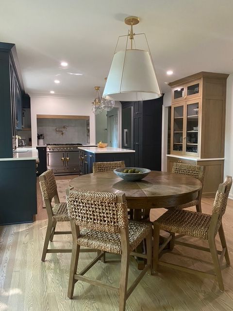 A modern kitchen dining area featuring a round wood table with four woven chairs under a large, white pendant light.
