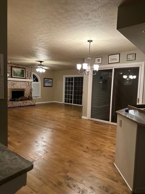 Spacious room with wood floors, a brick fireplace, sliding glass doors, and a chandelier, viewed from a kitchen counter. Spacious room with wood floors, a brick fireplace, sliding glass doors, and a chandelier, viewed from a kitchen counter.