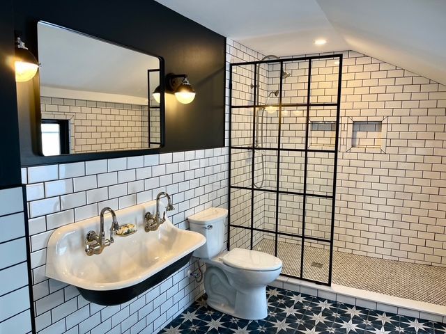 A bathroom with a wall-mounted double sink, dark accent wall, subway tiles, grid-style glass shower, and patterned floor. A bathroom with a wall-mounted double sink, dark accent wall, subway tiles, grid-style glass shower, and patterned floor.