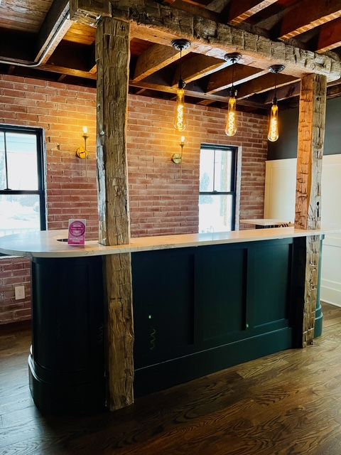 A dark green curved bar with a white countertop features rustic wood pillars and pendant lights against a brick wall. A dark green curved bar with a white countertop features rustic wood pillars and pendant lights against a brick wall.
