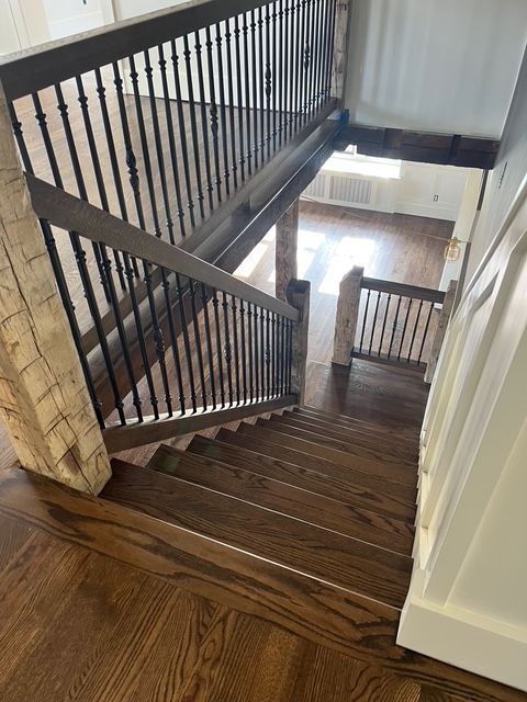 A high-angle view down dark wooden stairs with black metal railings, leading into a bright, open lower-level living area. A high-angle view down dark wooden stairs with black metal railings, leading into a bright, open lower-level living area.