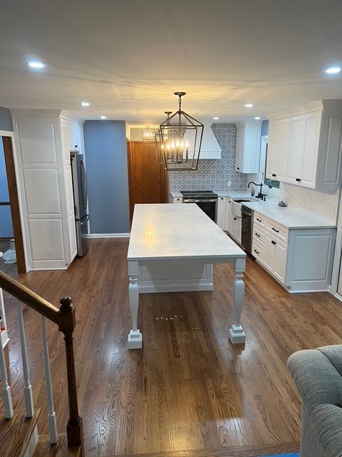 A bright, modern kitchen with white cabinets, a large central island, stainless appliances, and polished hardwood floors.