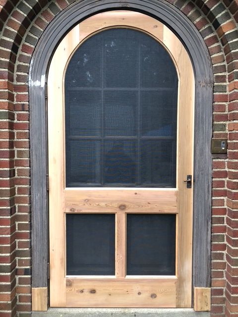 An arched wooden screen door installed in a brick doorway. An arched wooden screen door installed in a brick doorway.
