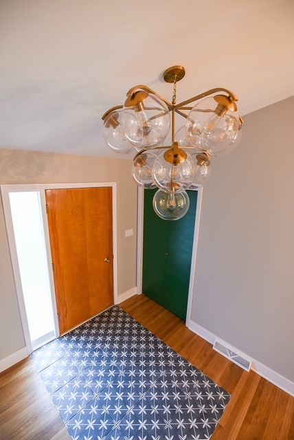 A high-angle view of a foyer with wood floors, a blue patterned rug, a wood door, a green door, and a globe chandelier. A high-angle view of a foyer with wood floors, a blue patterned rug, a wood door, a green door, and a globe chandelier.