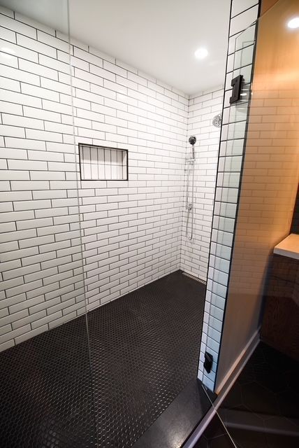 A walk-in shower with white subway tile walls, a small recessed niche, and a dark textured floor behind a glass door. A walk-in shower with white subway tile walls, a small recessed niche, and a dark textured floor behind a glass door.