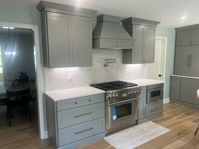 A modern kitchen with grey cabinetry, a stainless steel stove, and a marble-tiled backsplash under warm lighting.