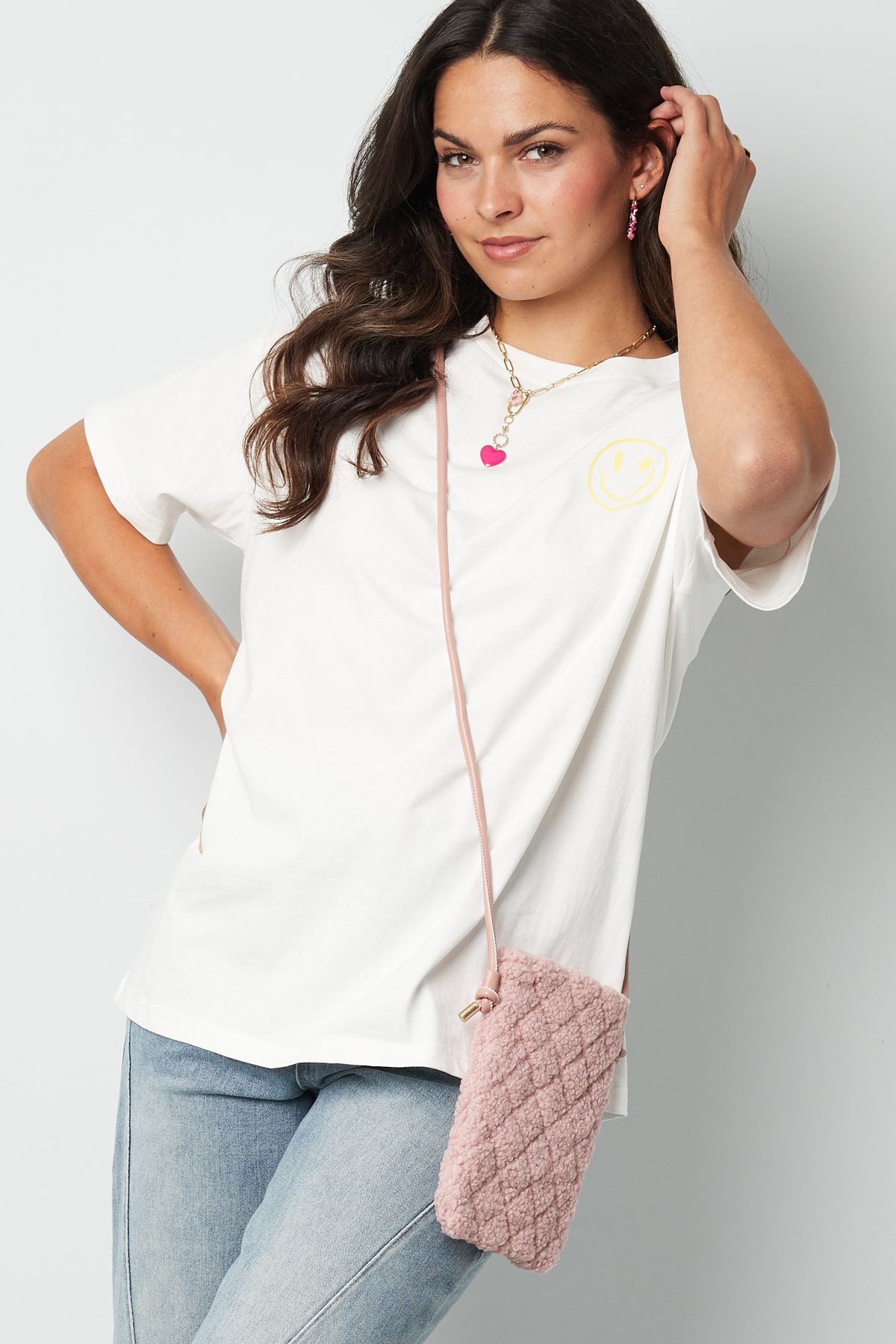 Een vrouw draagt ​​een wit T-shirt en een spijkerbroek en houdt een roze handtas vast.