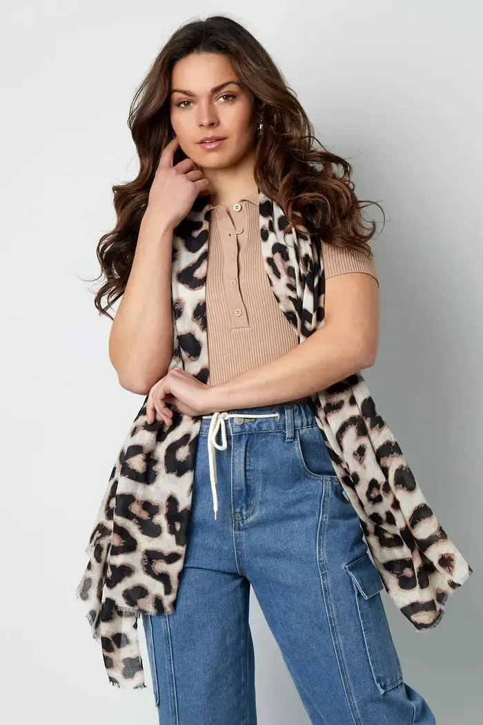 Een vrouw draagt ​​een luipaardprint vest en jeans.