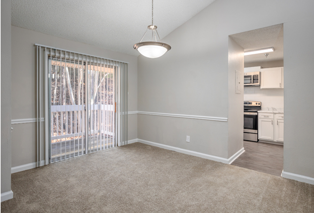 An empty living room with a sliding glass door and a chandelier.
