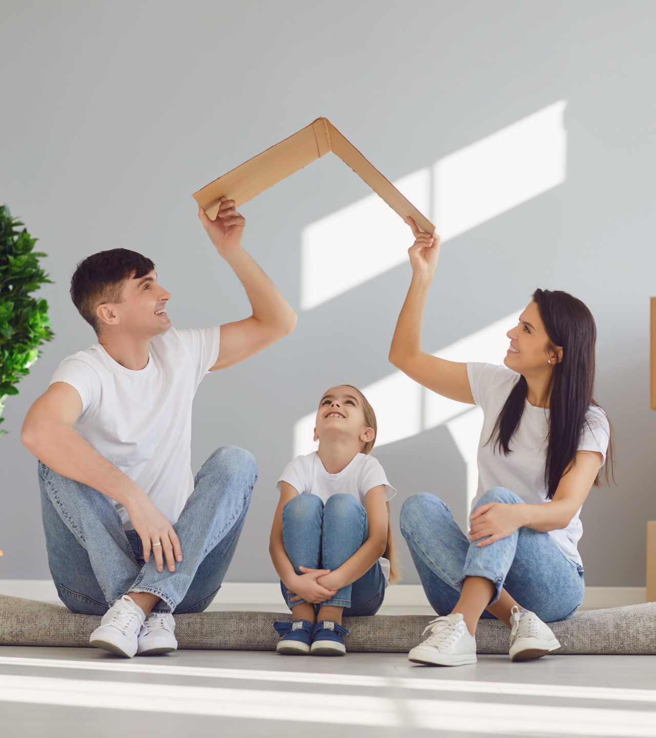 Three people sitting on a floor, holding wooden blocks together to form a house shape