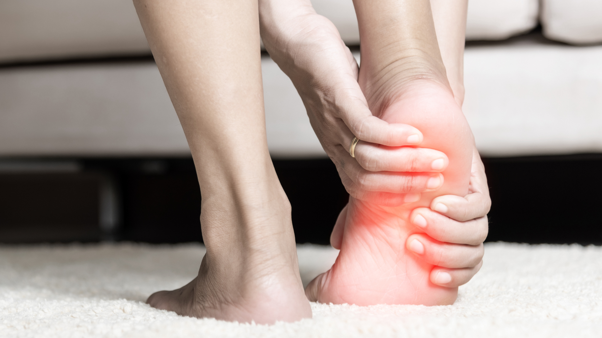 Woman holding her heel, indicating pain with red highlight on the affected area.