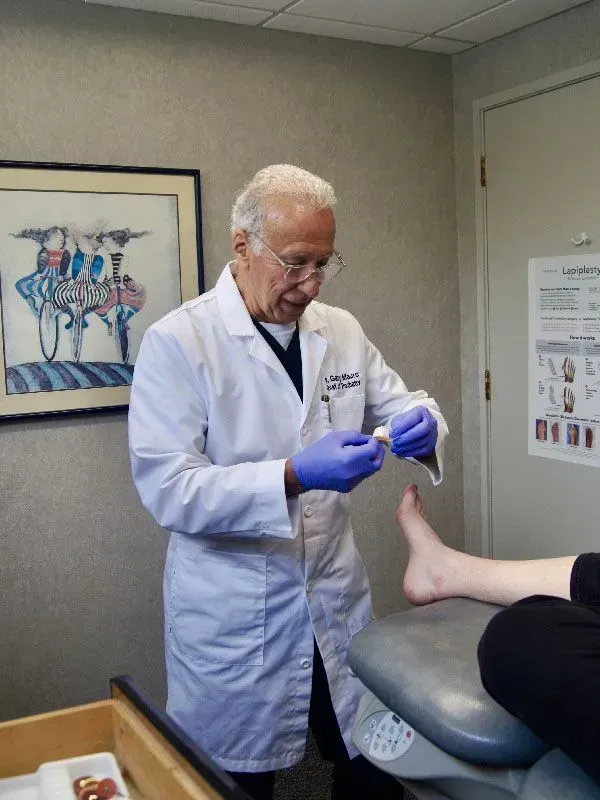 Doctor examining a patient's foot. He wears a lab coat and gloves. Interior office setting.