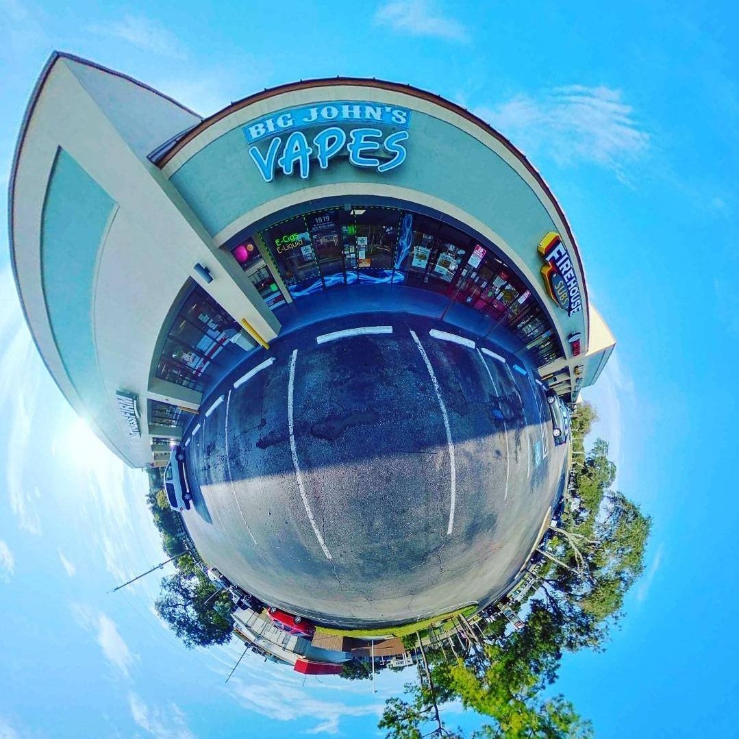 Tiny planet view of a vape shop storefront under a bright blue sky, with trees and street reflections.