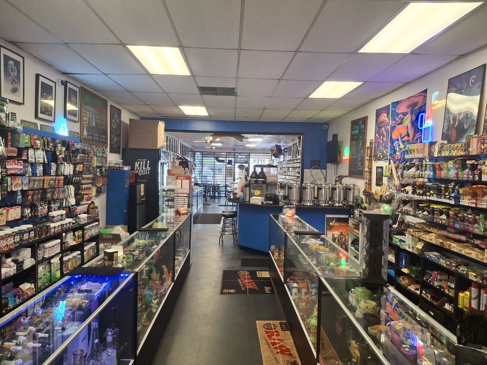 Comic and game store aisle with glass display cases, shelves of collectibles, and bright fluorescent lighting.
