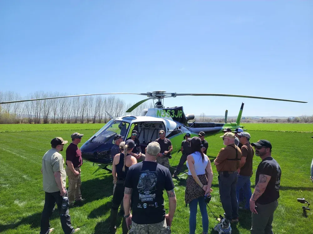 People gathered around a helicopter on a grassy field under a clear blue sky.