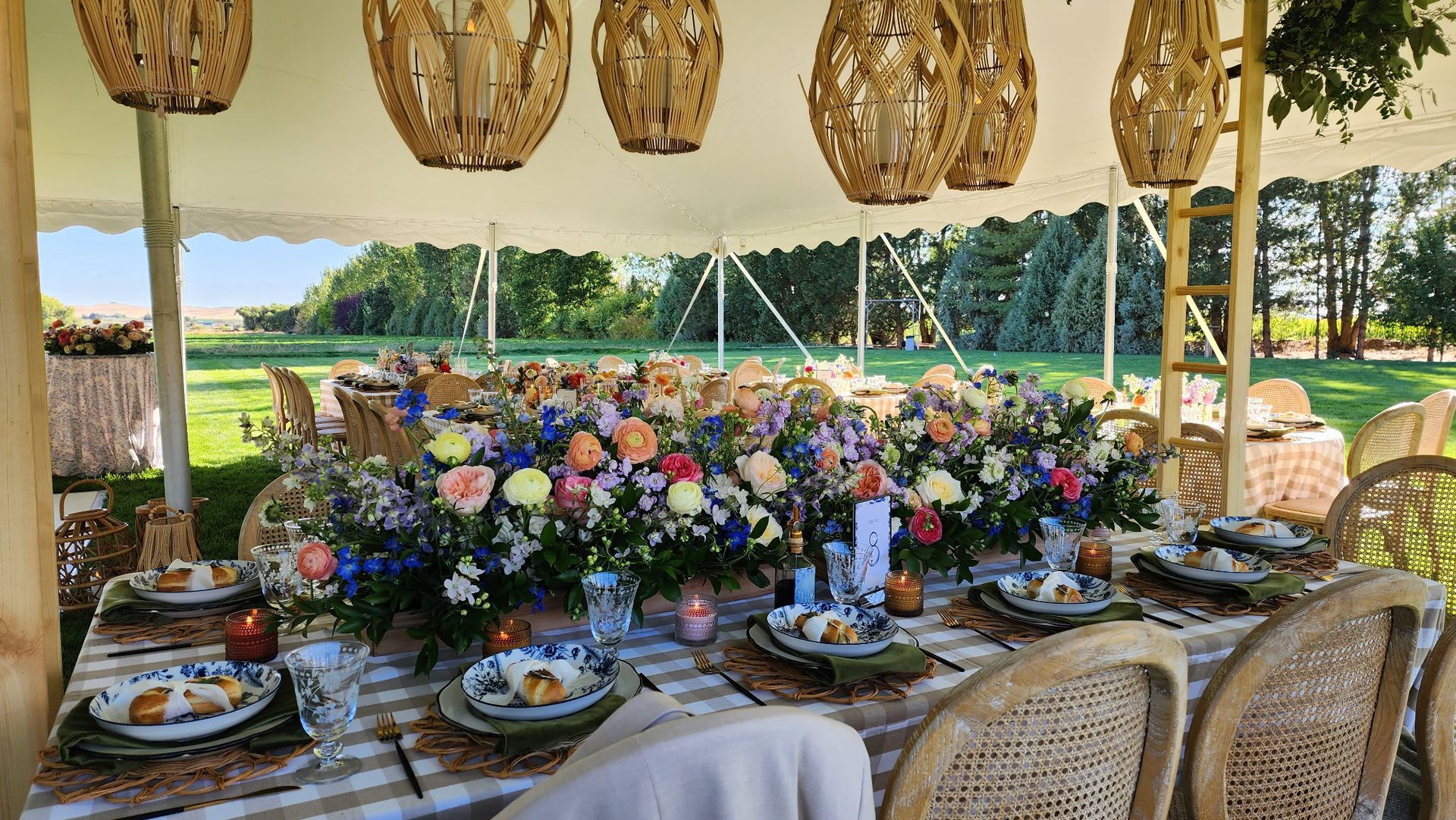 Elegant outdoor table set with flowers, candles, and woven chairs overlooking a lake and trees