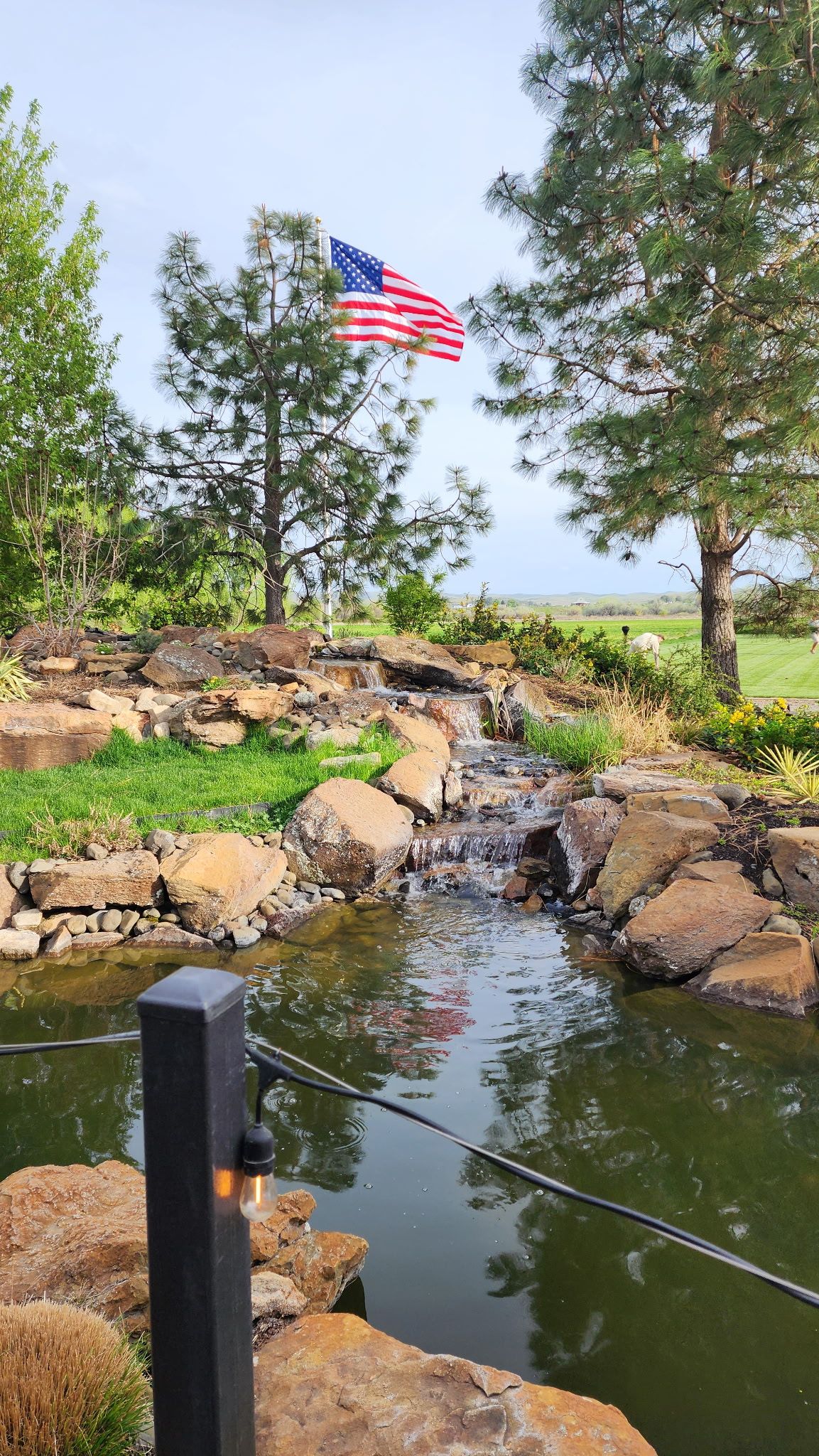 Rocky stream with a small waterfall, green trees, and an American flag waving above the water.