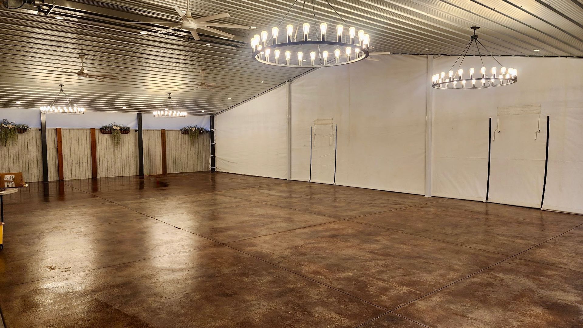 Empty banquet hall with polished wooden floor, white walls, and modern chandeliers under a patterned ceiling