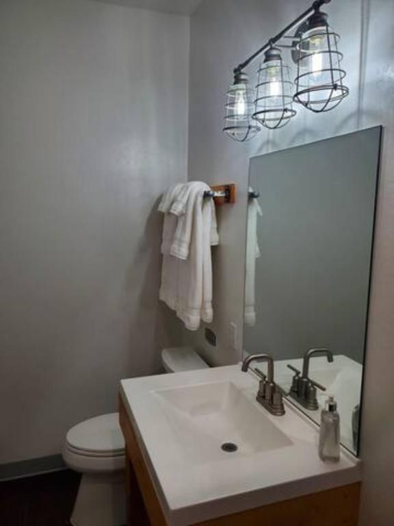 Modern bathroom vanity with sink, mirror, towel rack, toilet, and three hanging light fixtures