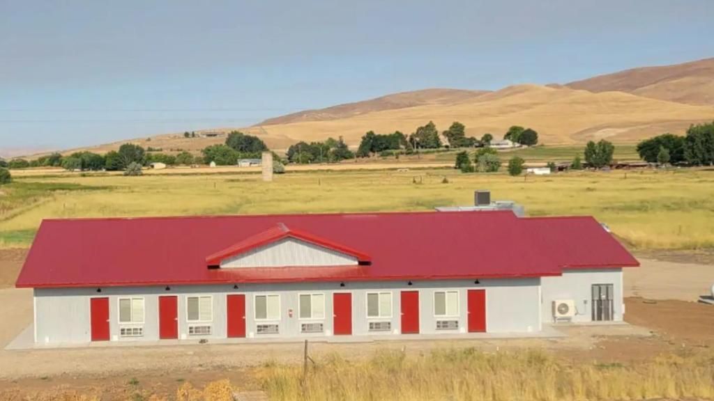 Single-story white building with a red roof in a dry rural landscape with hills.