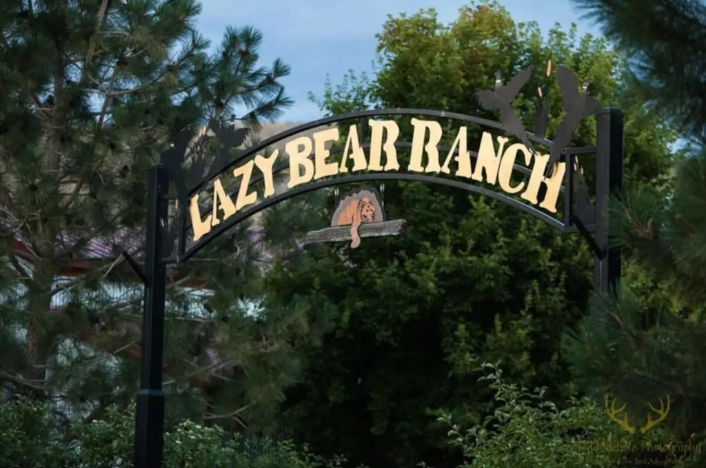 Entrance sign reading “Lazy Bear Ranch” on an arched black gate, surrounded by trees.