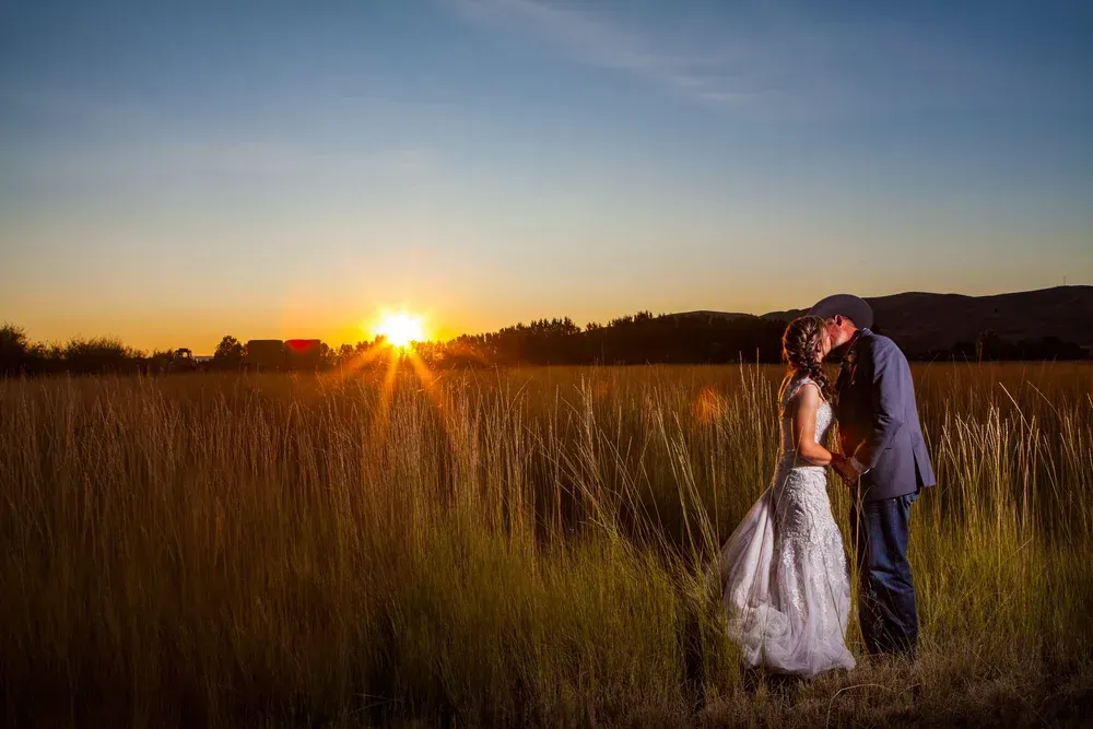 Couple embracing in a grassy field at sunset, with a white dress and golden sky.