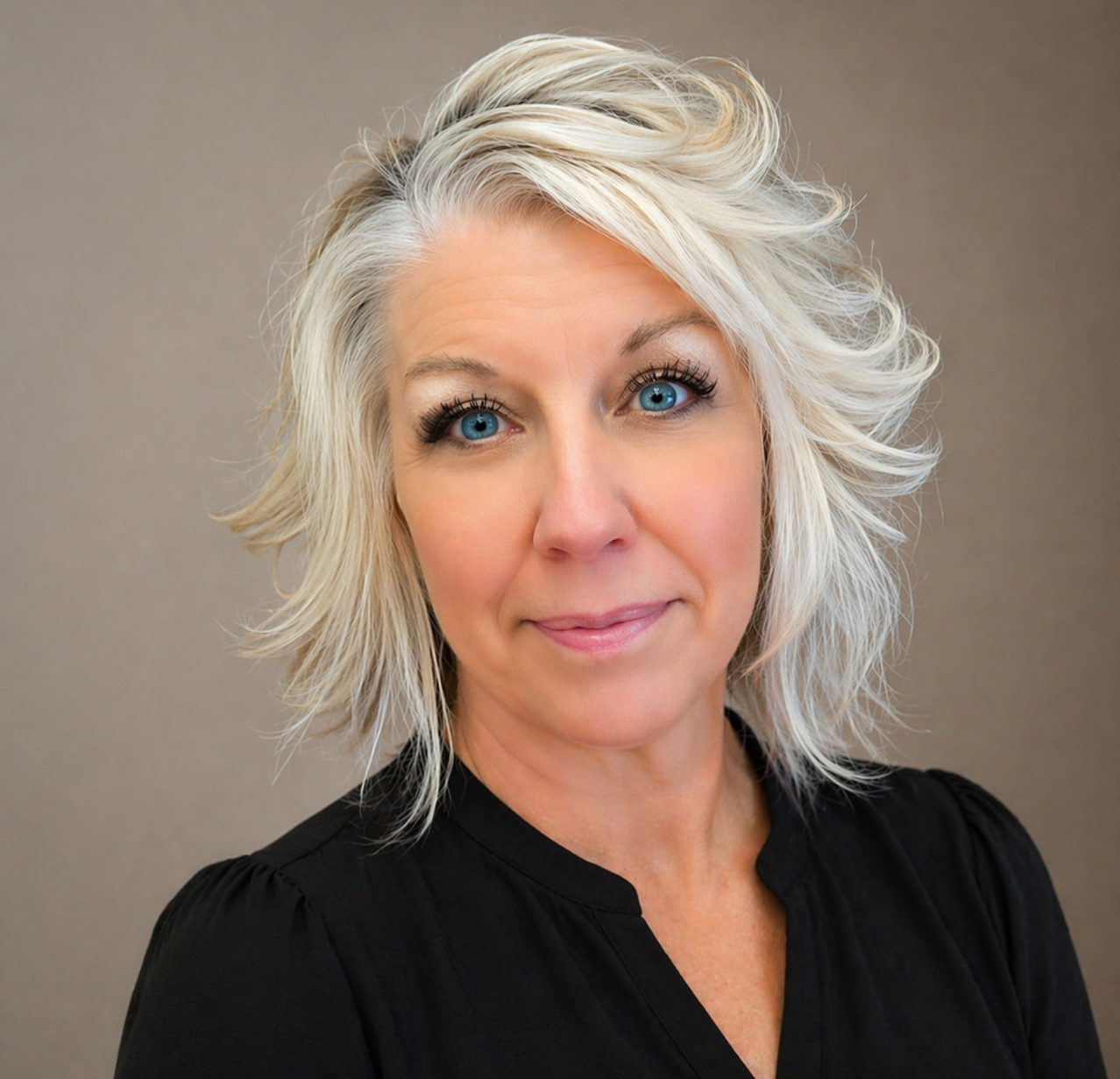 Portrait of a woman with short silver hair, wearing a black top against a neutral gray background