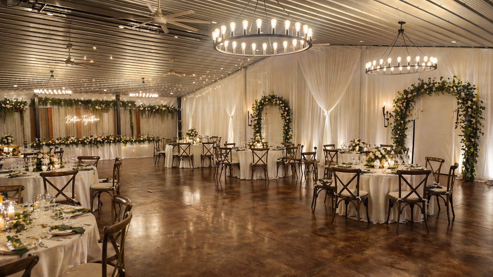 Elegant banquet hall with round tables, white draping, chandeliers, and floral arch decor