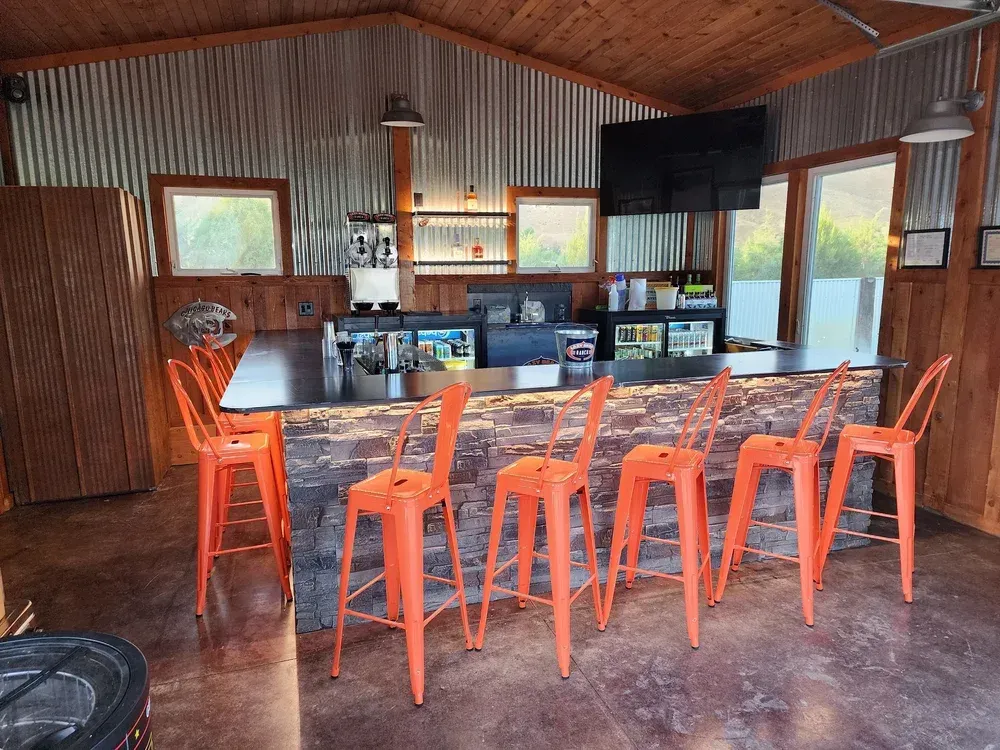 Rustic cabin bar with orange stools, counter seating, and large windows overlooking water