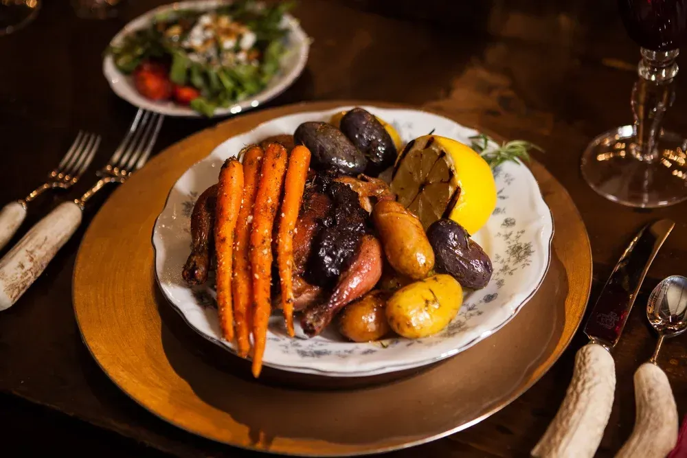 Plated roasted vegetables and meat on a dining table with utensils and a glass nearby