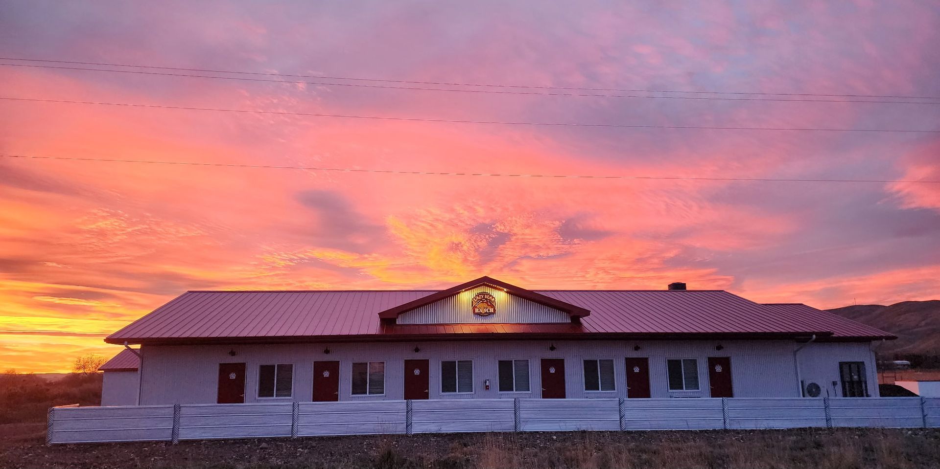 Single-story white building at sunset beneath a pink-orange sky