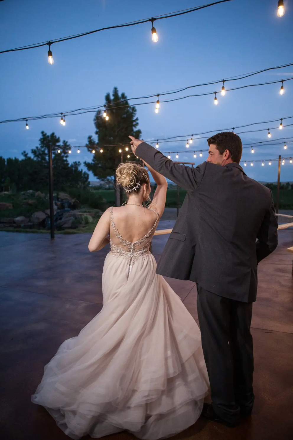 Bride and groom dancing outdoors under string lights at dusk