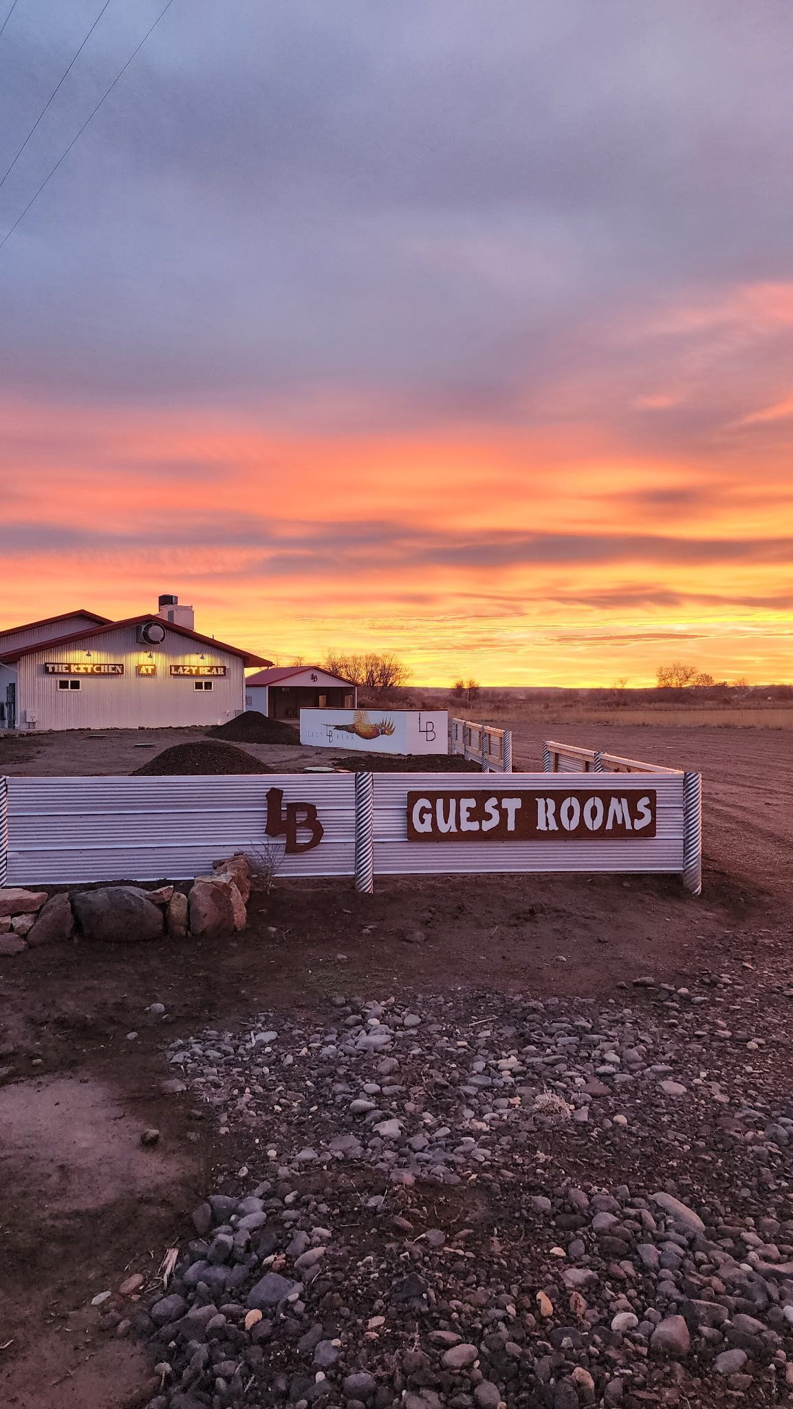 Rustic guest house sign at sunset, with a purple-orange sky over a rocky foreground