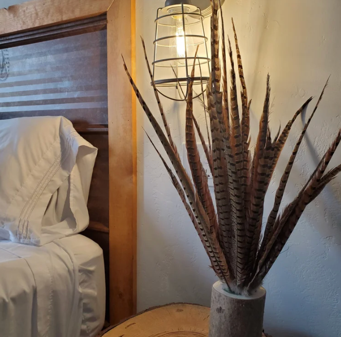 Bedroom corner with bed, wall sconce, and a tall vase of dried reeds on a small table