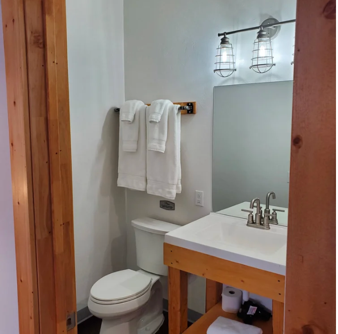 Small bathroom with toilet, vanity sink, mirror, and towels on a white wall