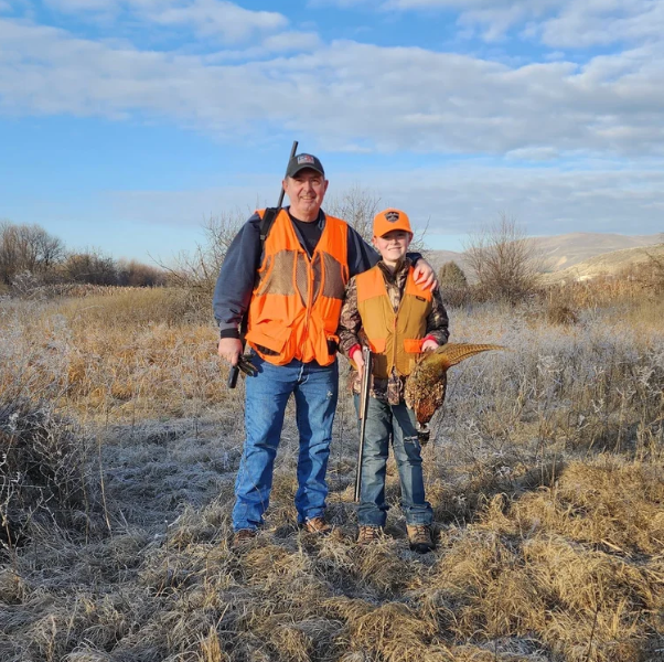 Two hunters in orange safety vests standing in a frosty field under a cloudy sky