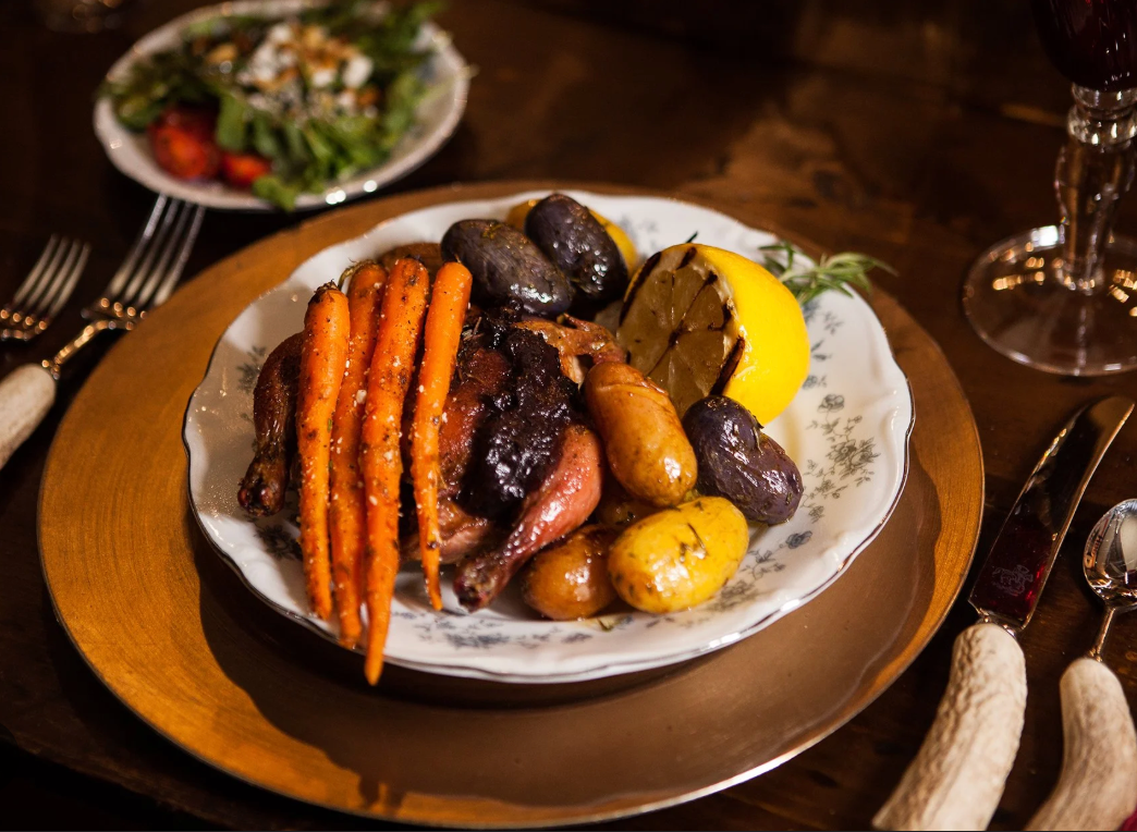 Roasted chicken and vegetables on a white plate at a restaurant table