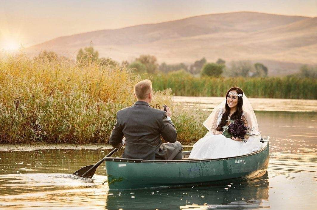 Couple in a canoe on a calm lake at sunset, with reeds and mountains in the background.