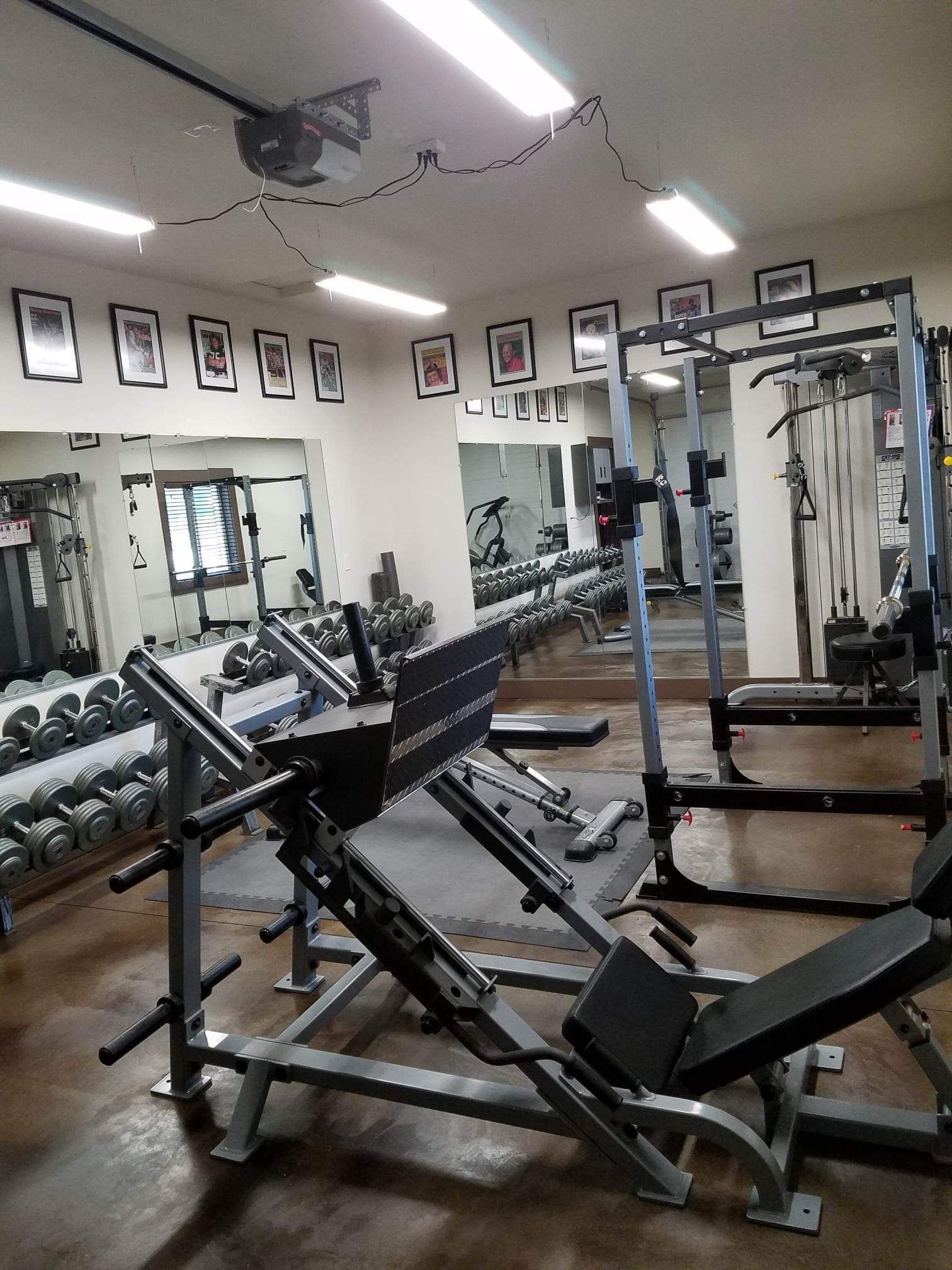 Gym interior with weight machines, dumbbells, mirrors, and benches under bright ceiling lights