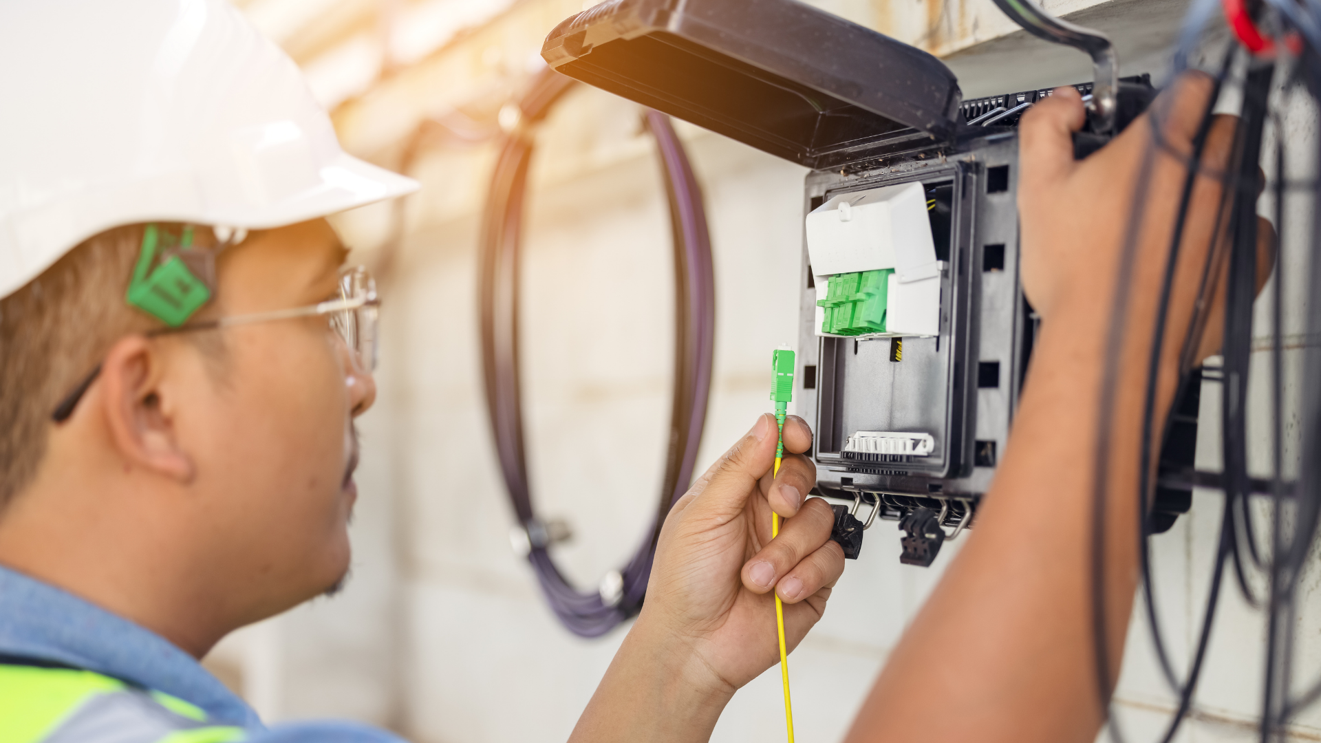 Technician wiring an electrical panel in a wall with tools and cables visible
