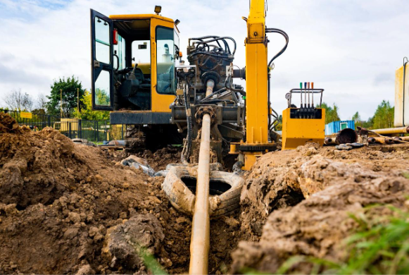 Horizontal directional drilling machine installing underground pipe through soil at a construction s
