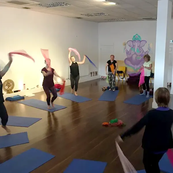 A yoga group enjoying a fun workshop waving scarves in a beautiful studio.