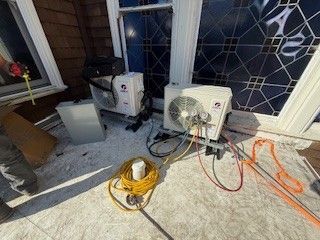 Outdoor porch with HVAC equipment, coiled orange hose, and a yellow extension cord on the floor