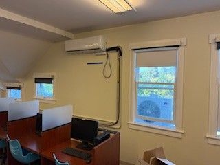 Small office with desks, computers, and windows under wall-mounted air conditioners