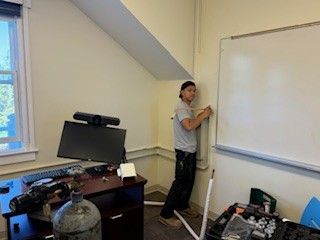 Person writing on a whiteboard in an office, with a desk and computer in the foreground.