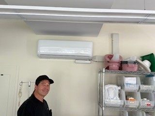 Person standing in a storage room beside metal shelving and pink bins under a wall-mounted air conditioner